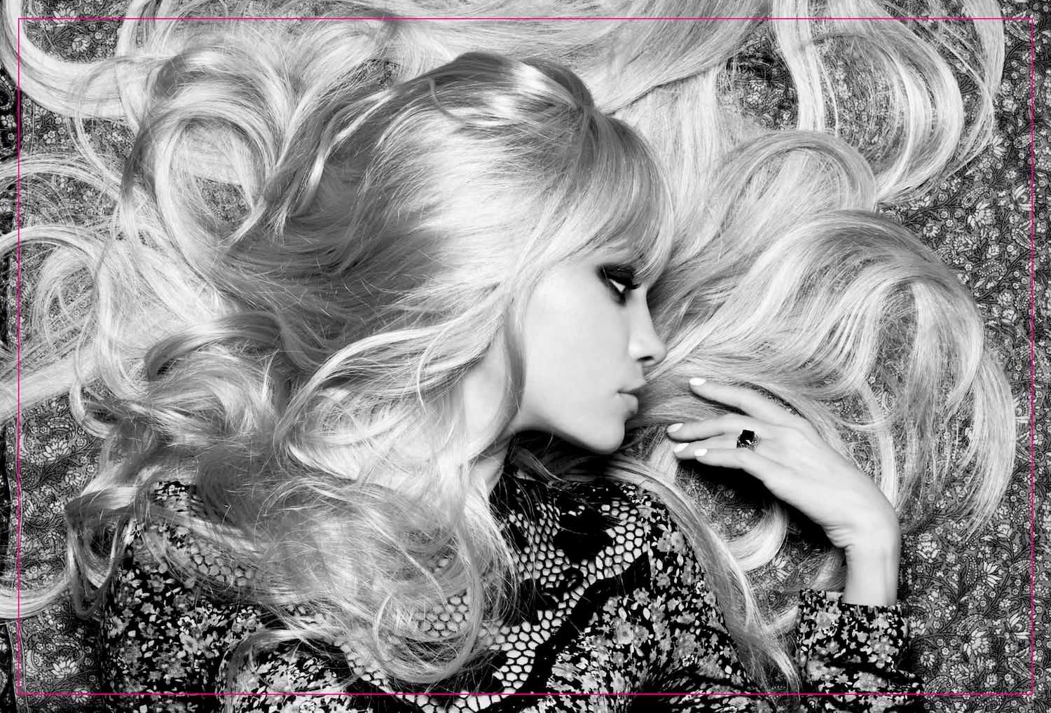 Blonde woman with voluminous hair lying on patterned backdrop.