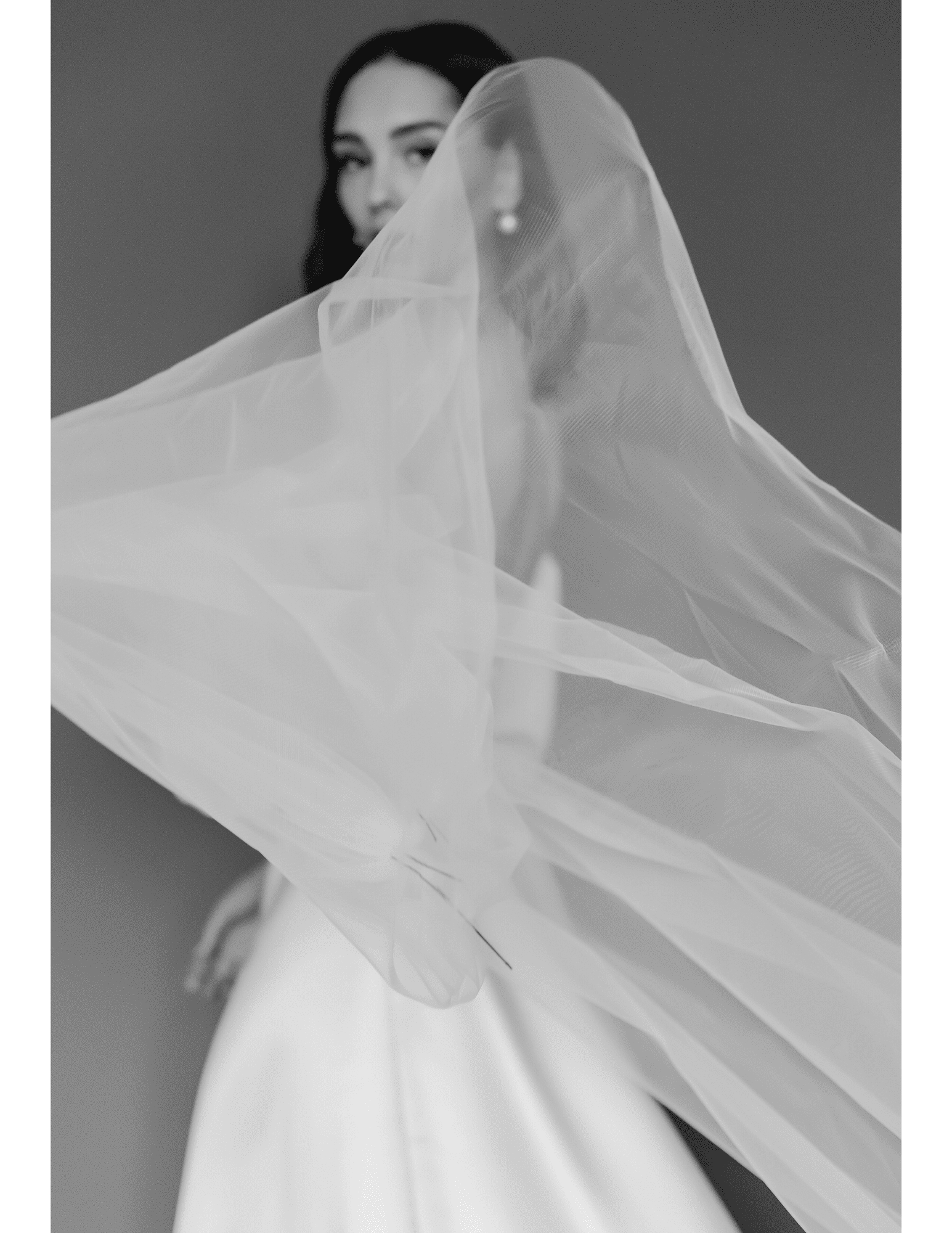 Bride posing, holding a flowing veil gracefully in black-and-white photograph.